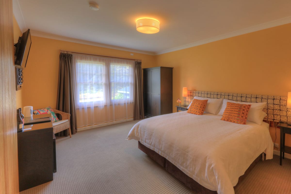 A hotel room with a large bed, a desk, a chair, a wardrobe, and a window with curtains.