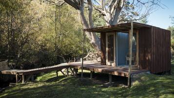 A rustic wooden cabin with a deck, surrounded by trees and a clear sky.