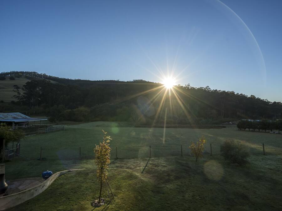 Paisatge rural amb cel blau, sol baix a l'horitzó i un camp tancat per una tanca.