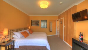 A hotel room with a large bed, a television mounted on the wall, and a door leading to the bathroom. - Ashdowns of Dover B&B (Dover)