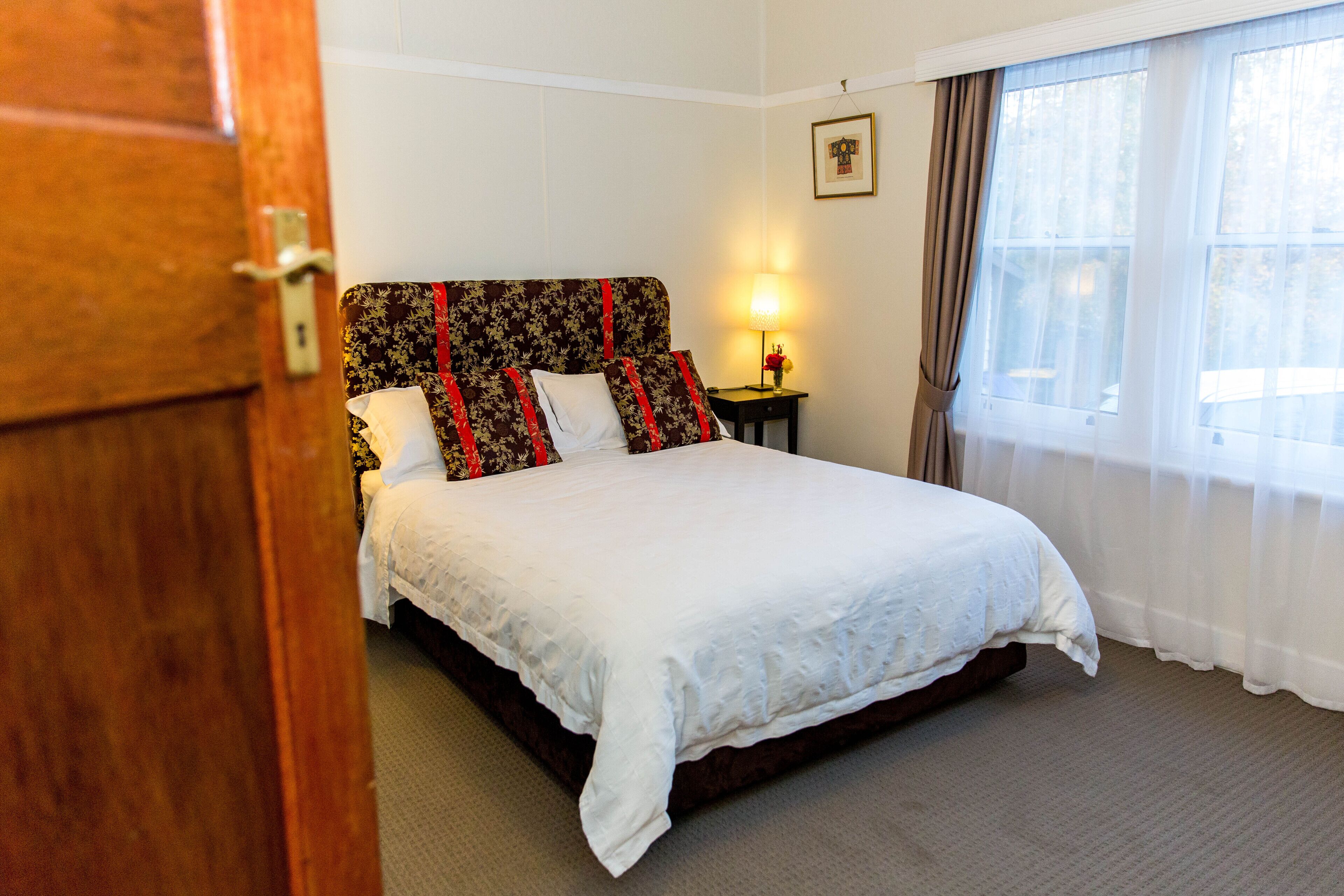 A neatly made bed with a floral headboard, a bedside lamp, and a window with curtains.