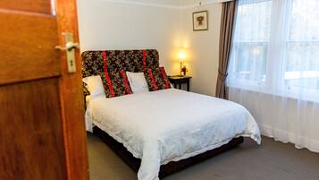 A neatly made bed with a floral headboard, a bedside lamp, and a window with curtains.