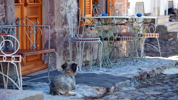 A rustic stone building with a wooden door and a metal table and chairs set outside.