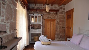 A bedroom with a stone wall, wooden ceiling, a bed with white linens, a wooden wardrobe, and a hanging light fixture.