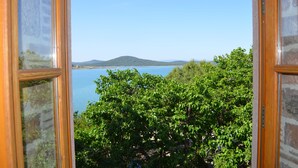A view through a window with a clear blue sky, a body of water, and a distant hill.