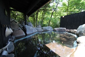 A tranquil outdoor hot spring area with a wooden deck, large rocks, and a clear pool surrounded by lush greenery. - Yufuin Ryoan Wazanhou (Yufu)
