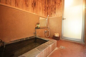 A bathroom with a stone bathtub, wooden paneling, a mirror, and a shower. - Yufuin Ryoan Wazanhou (Yufu)