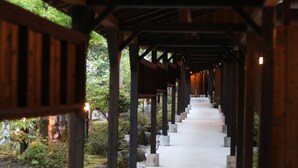 A covered walkway with wooden beams and stone bases, surrounded by greenery and rocks. - Yufuin Ryoan Wazanhou (Yufu)