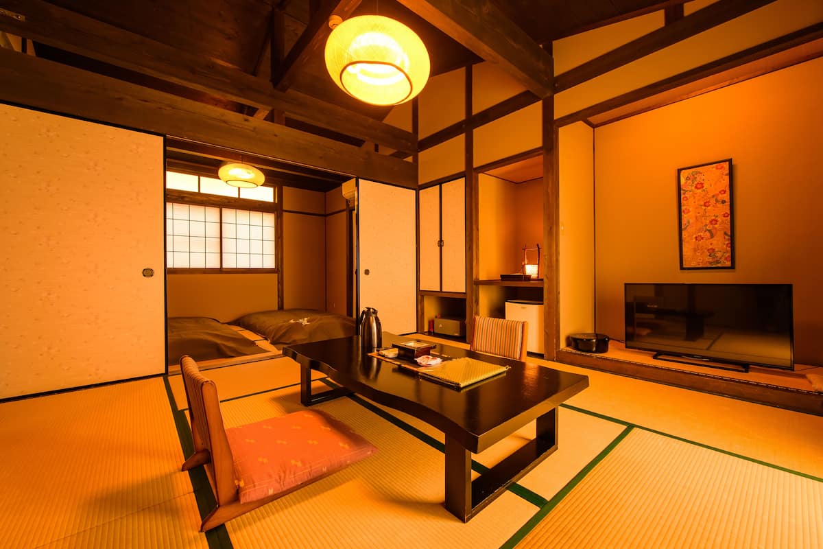 A traditional Japanese room with tatami flooring, a low table, a sofa, and a television.