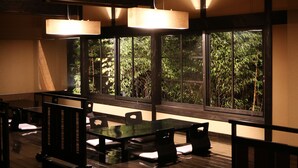A room with a wooden table and chairs, large windows with a view of greenery, and hanging light fixtures. - Yufuin Ryoan Wazanhou (Yufu)