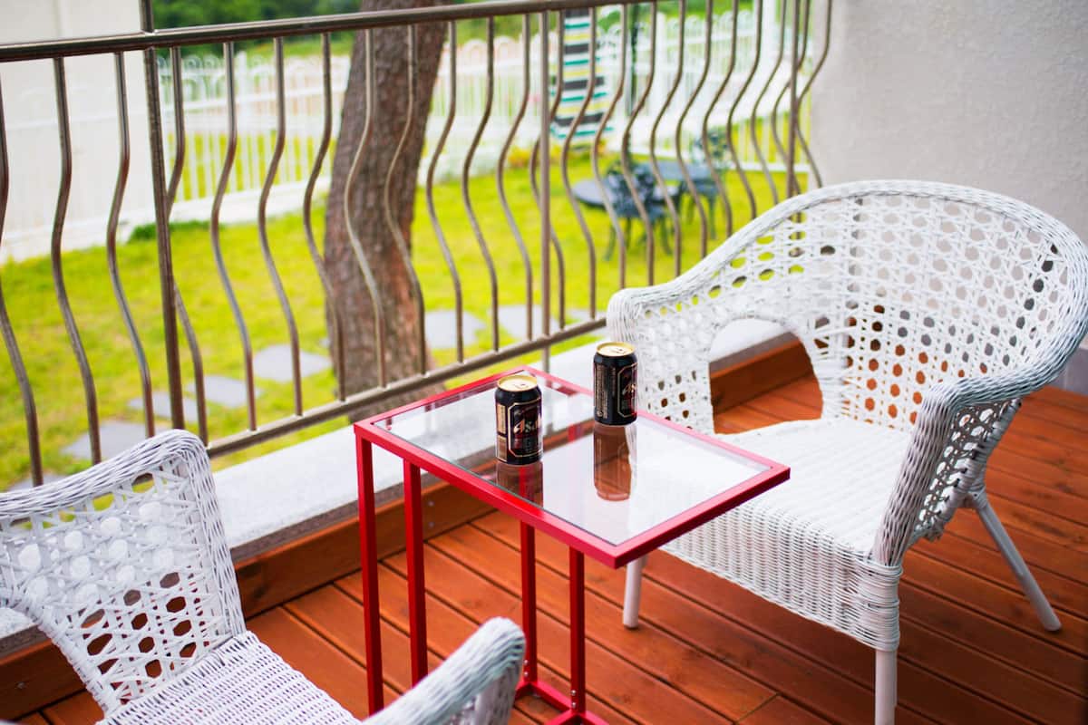 A balcony with wicker chairs, a small table, and two cans of beer.