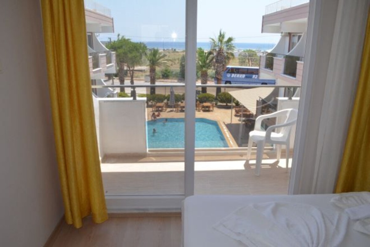 A hotel room with a balcony overlooking a swimming pool and a view of the beach.