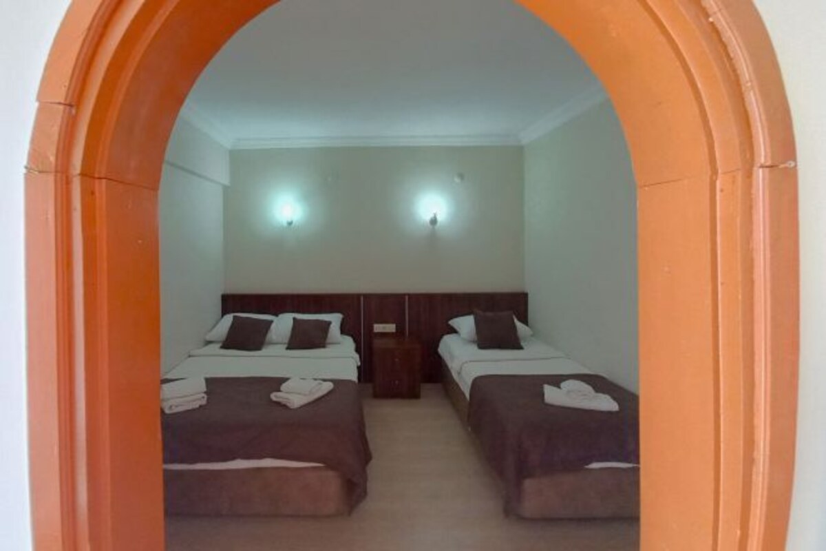 A room with two beds, each with a headboard and pillows, and a nightstand between them.