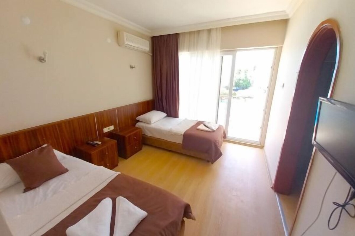 A hotel room with two beds, a TV, a wooden floor, and a view of the outdoors through a sliding door.