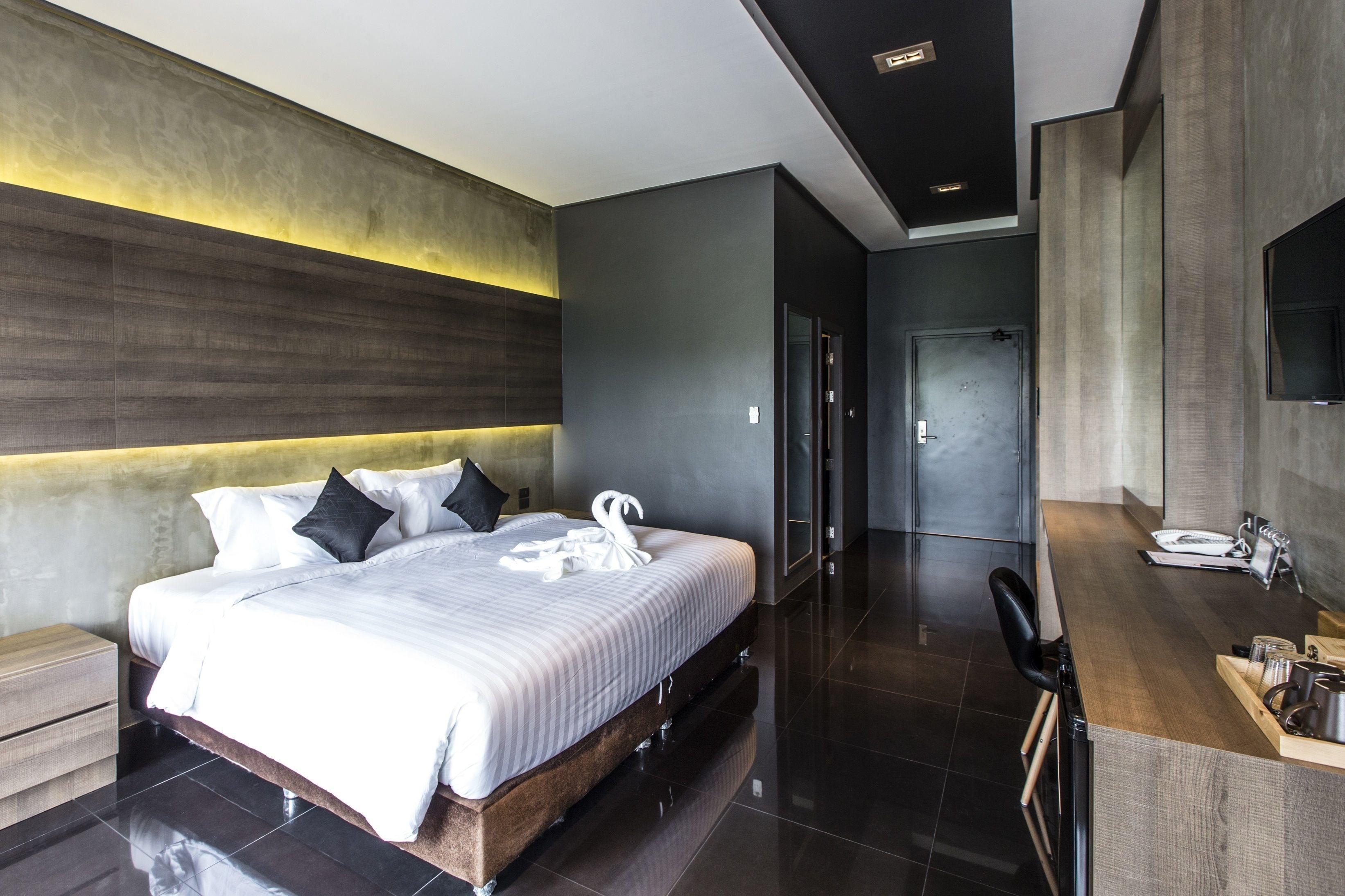 Una habitación de hotel moderna con una cama grande, un cabecero de madera, un escritorio empotrado y un espejo.
