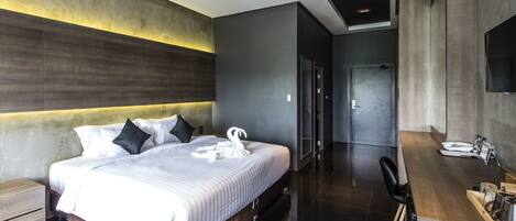 Una habitación de hotel moderna con una cama grande, un cabecero de madera, un escritorio empotrado y un espejo.