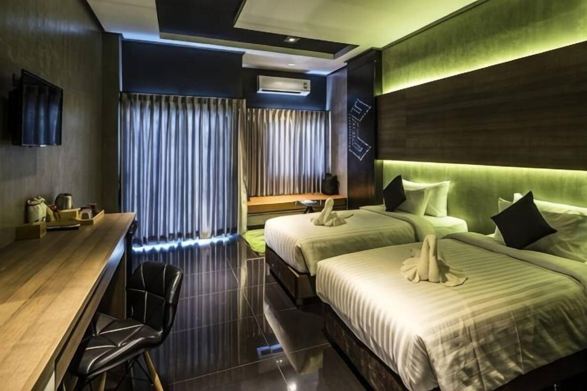 A hotel room with a desk, two beds, a TV, and a window with curtains.