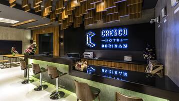 A hotel reception area with a modern design, featuring a reception desk, seating area, and a large illuminated sign displaying the hotel name.