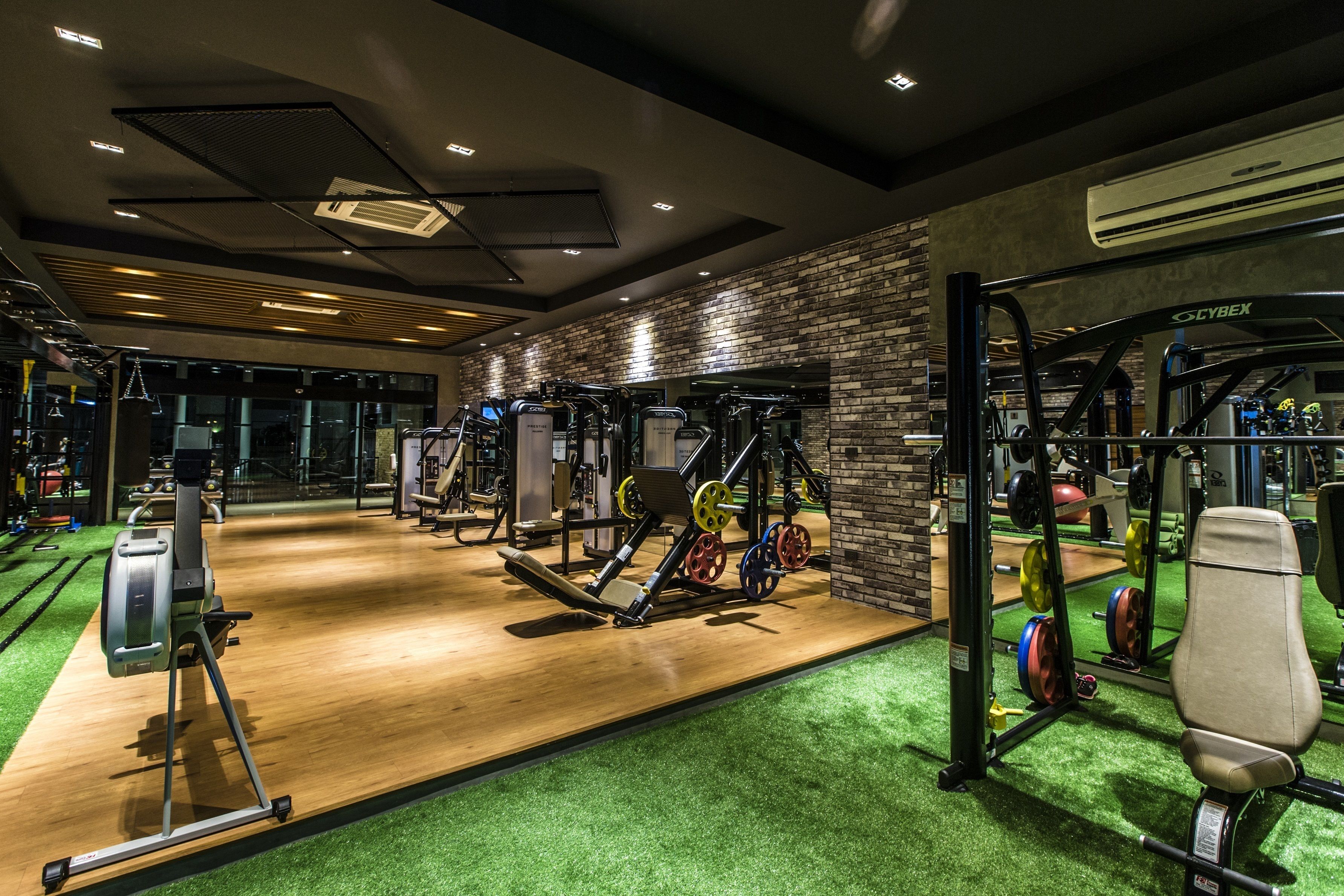 A gym with various exercise equipment, a wooden floor, and green artificial turf.
