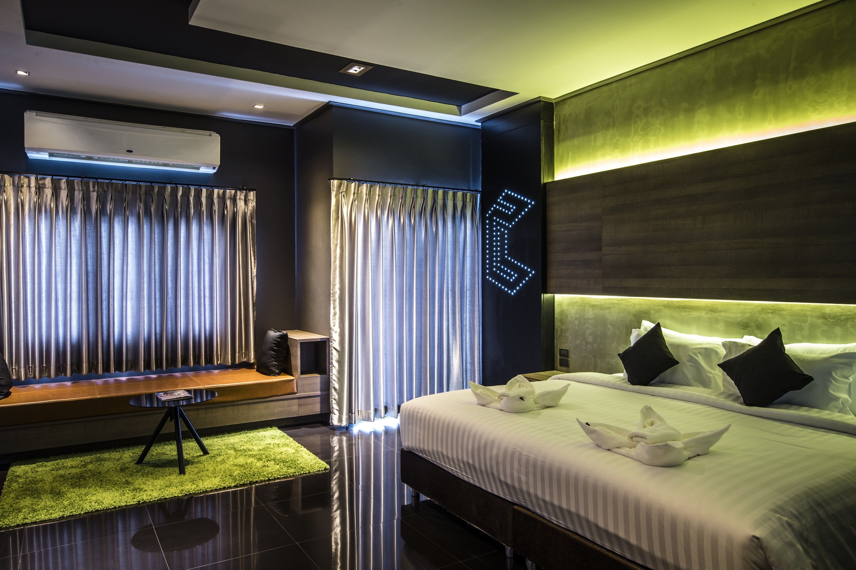 Una habitación de hotel moderna con una cama grande, un área de descanso con una mesita y un ventanal con cortinas.