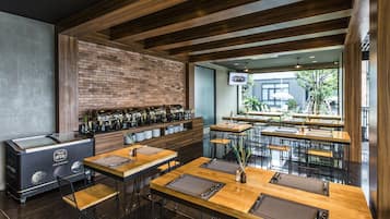 Una cafetería moderna con mesas y sillas de madera, una pared de ladrillo y un ventanal grande con vistas a la calle.