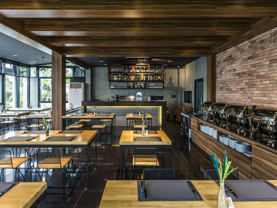 Un restaurante moderno con mesas y sillas de madera, una zona de bar con estantes llenos de botellas y una pared de ladrillo.