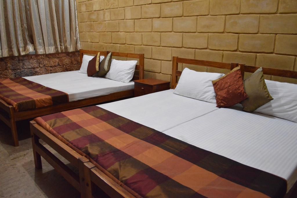 Two single beds with wooden frames and white linens, a wooden bench, and a stone wall.