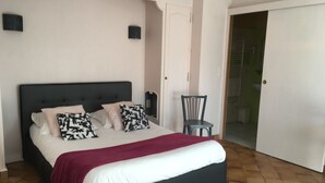 Un dormitorio con cama, almohadas, una silla, una puerta y suelo de baldosas.
