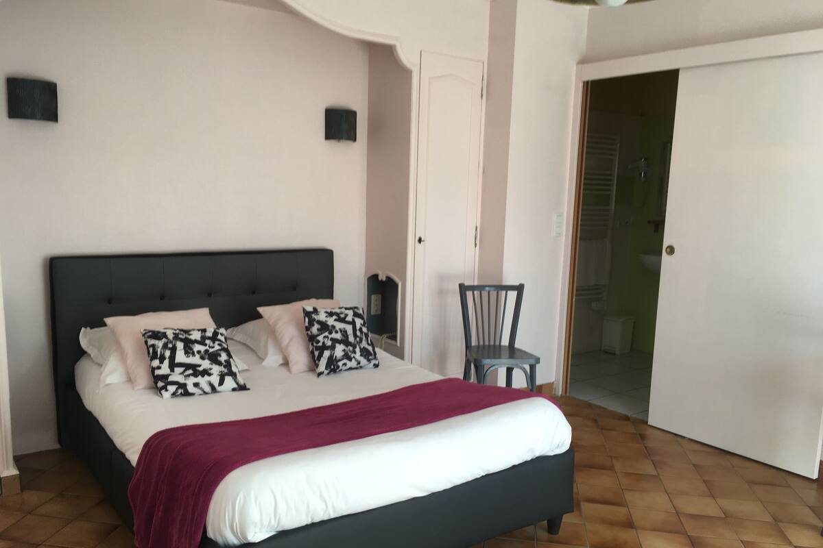 Une chambre à coucher avec un lit, des oreillers, une chaise, une porte et un sol carrelé.