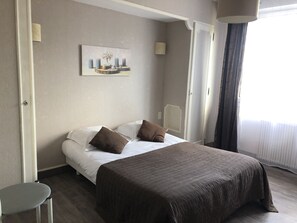 Habitación de hotel con cama, almohadas, un cuadro en la pared y ventana con cortinas.