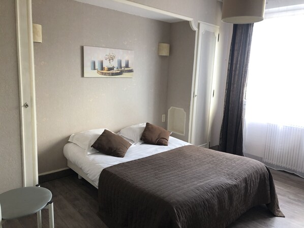 Habitación de hotel con cama, almohadas, un cuadro en la pared y ventana con cortinas.