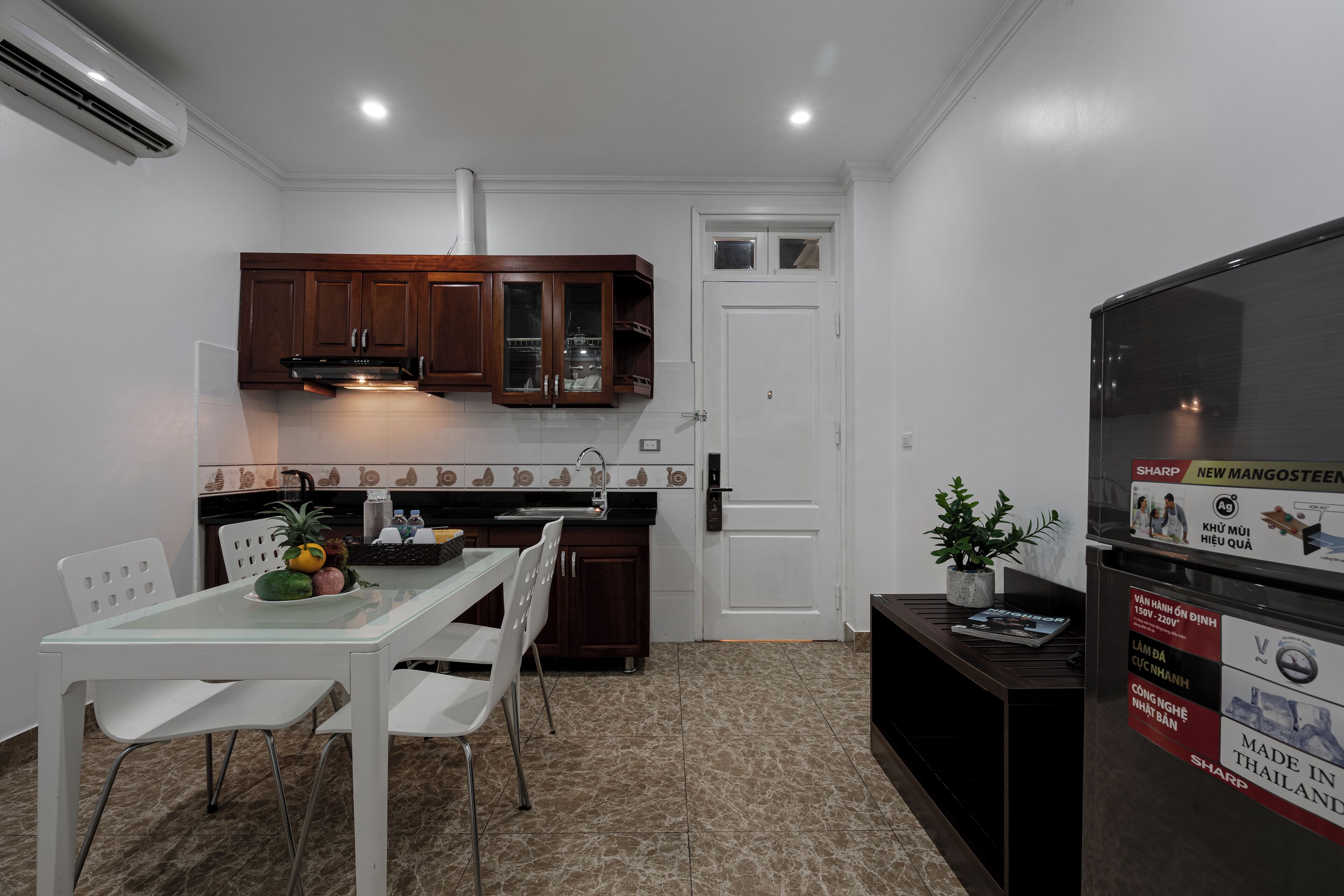 A compact kitchen with dark wooden cabinets, a white door, and a refrigerator with promotional stickers.