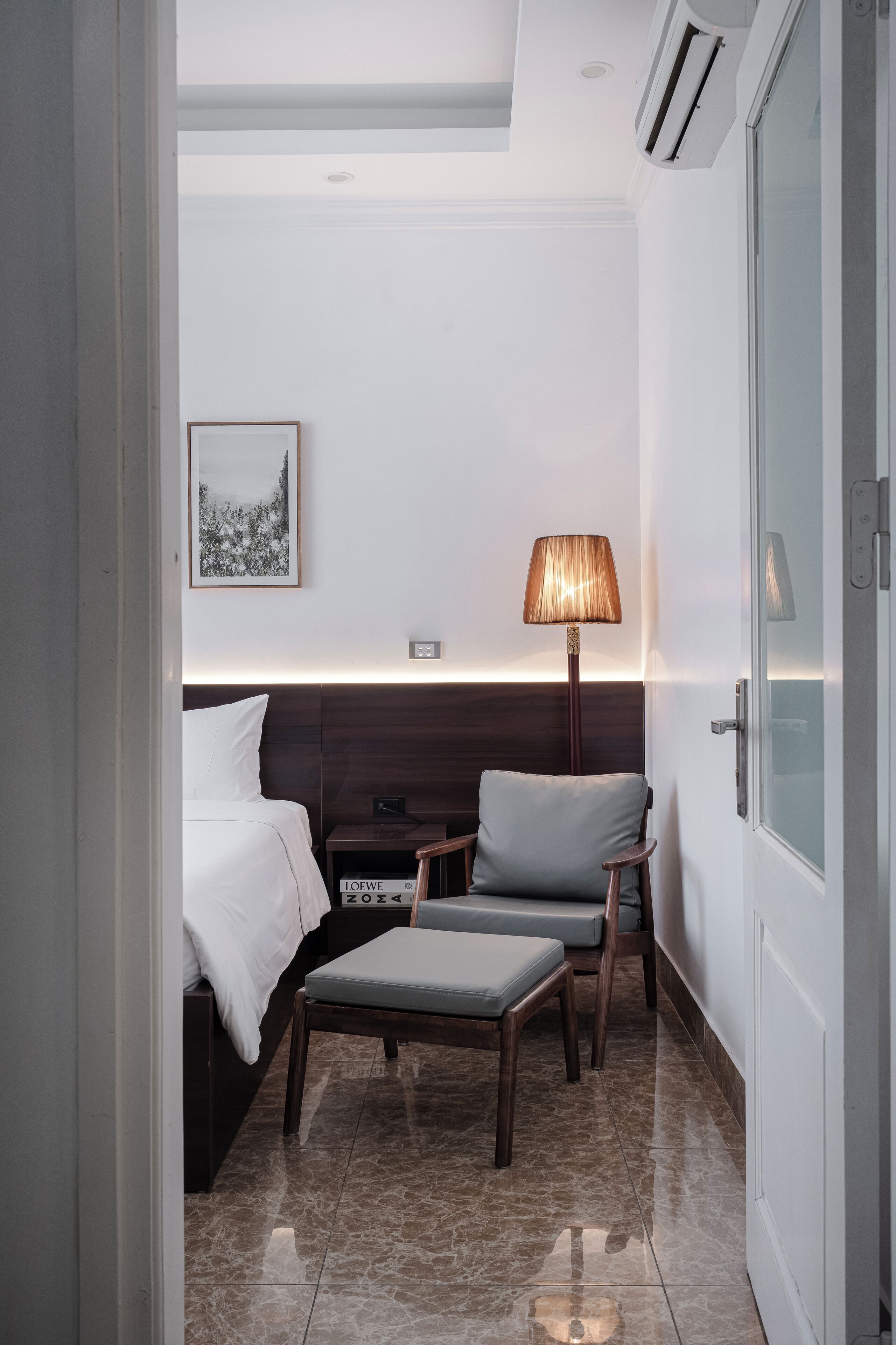 A hotel room with a bed, a desk, a chair, a lamp, and a framed picture on the wall.