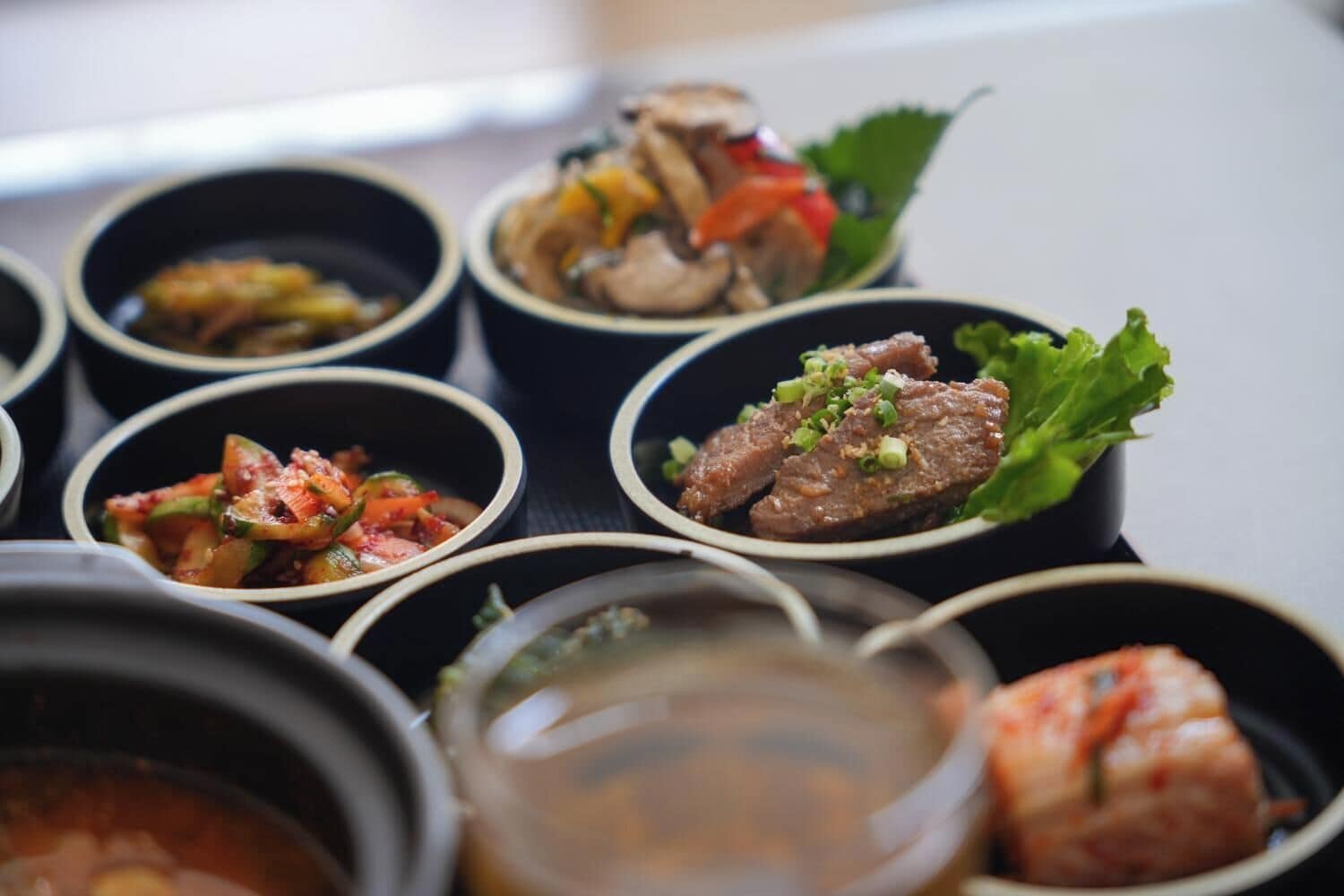 A variety of dishes in small bowls, including what appears to be a meat dish with green onions, a vegetable stir-fry, and a soup.