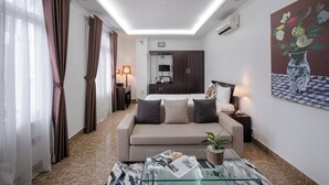 Quarto de hotel moderno com sofá, mesa de centro de vidro, cama, escrivaninha e um quadro na parede.