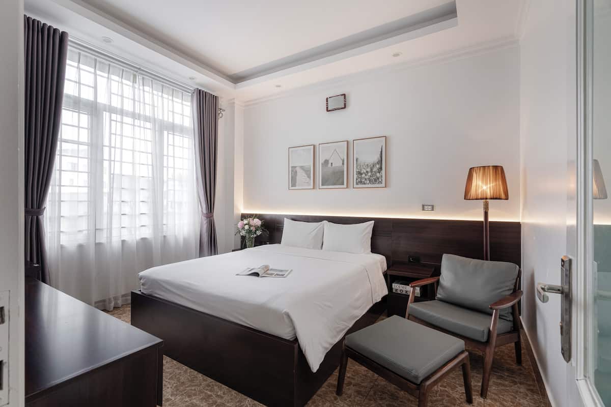 A hotel room with a large bed, a bedside table, a chair, a lamp, and a small table.