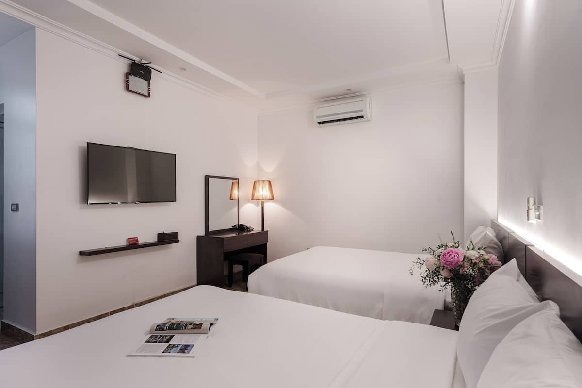 A hotel room with two beds, a TV, a desk with a lamp, and a wall-mounted air conditioner.