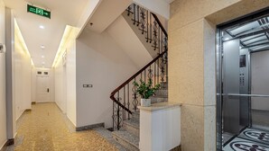 Um saguão de hotel moderno com piso de mármore, uma escadaria com grades decorativas e um elevador.