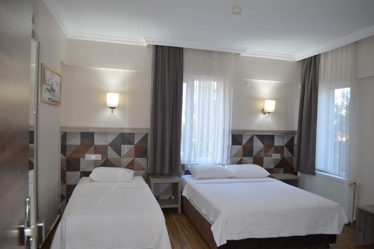 A hotel room with two beds, a tiled wall, a window with curtains, and wall-mounted lights.
