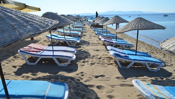 A beach with rows of sun loungers and thatched umbrellas. - Megas Hotel (Ayvalik)