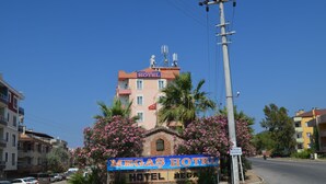 A hotel named "MEGAS HOTEL" with a signboard, surrounded by parked cars and palm trees. - Megas Hotel (Ayvalik)