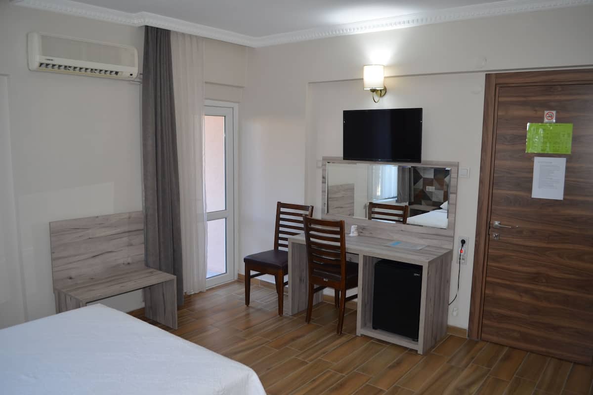 A hotel room with a bed, a desk with a chair, a television, and a door with a mirror.