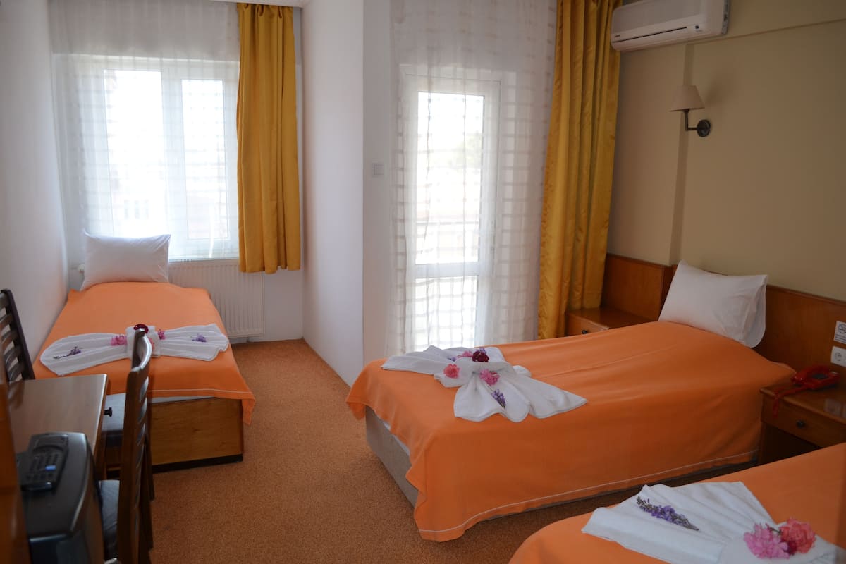 A hotel room with two beds, each with an orange bedspread and white pillows. There is a desk with a chair, a telephone, and a lamp on the wall.