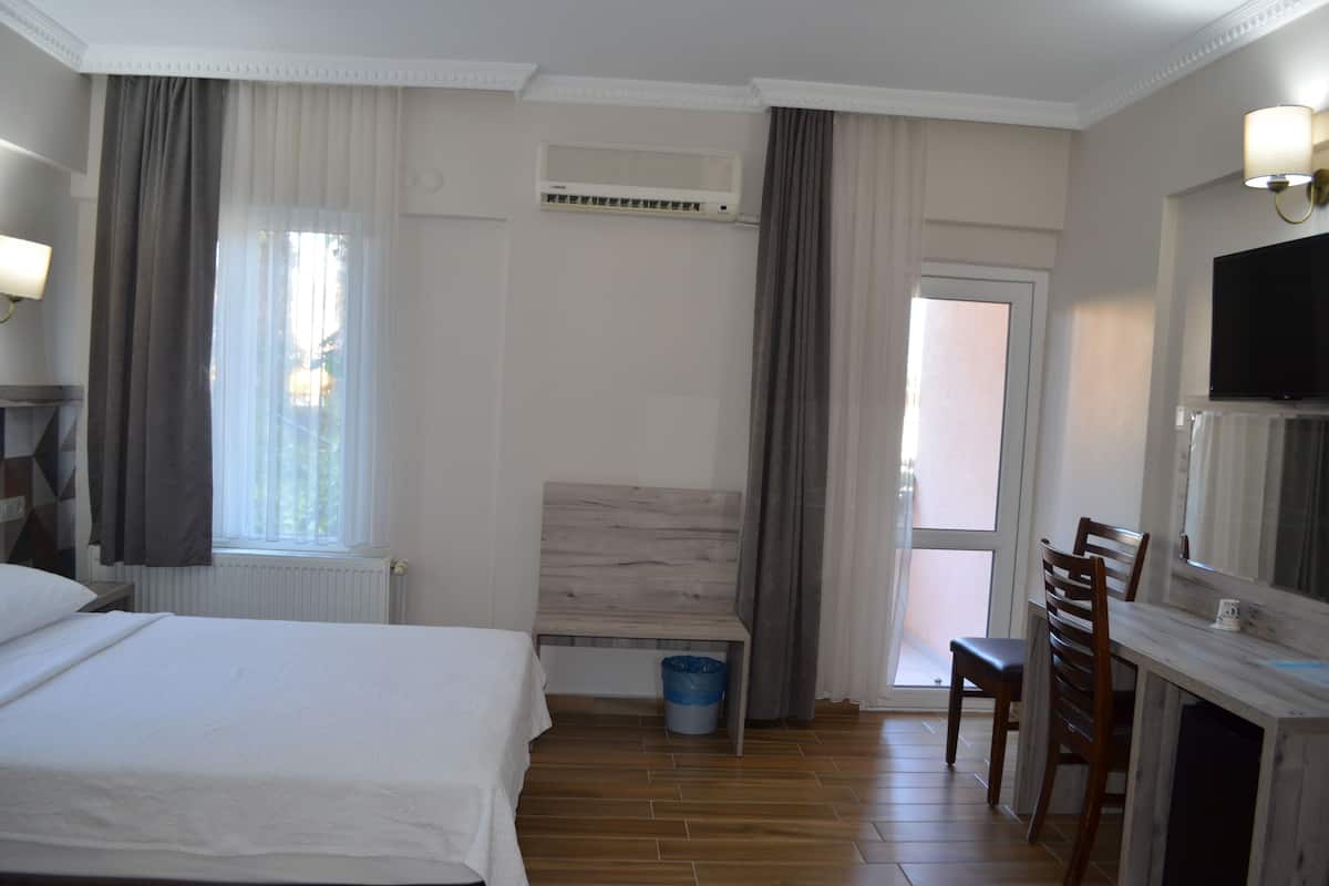 A hotel room with a bed, a desk, a chair, a TV, and a window with curtains.