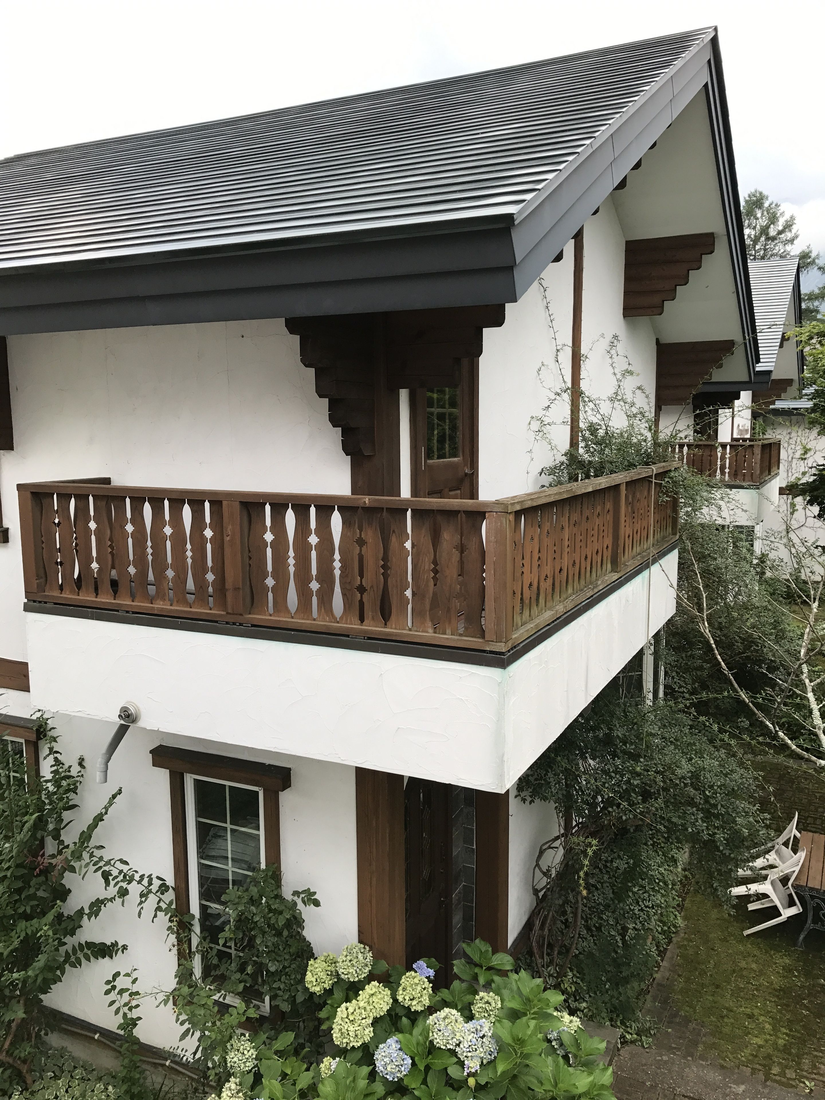 A two-story building with a balcony, a wooden fence, and a garden with hydrangea flowers.