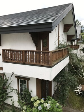 Un bâtiment à deux étages doté d’un balcon, d’une clôture en bois et d’un jardin où poussent des hortensias.