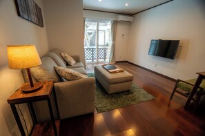Un salon comprenant un canapé, un pouf, une lampe et un téléviseur à écran plat fixé au mur.