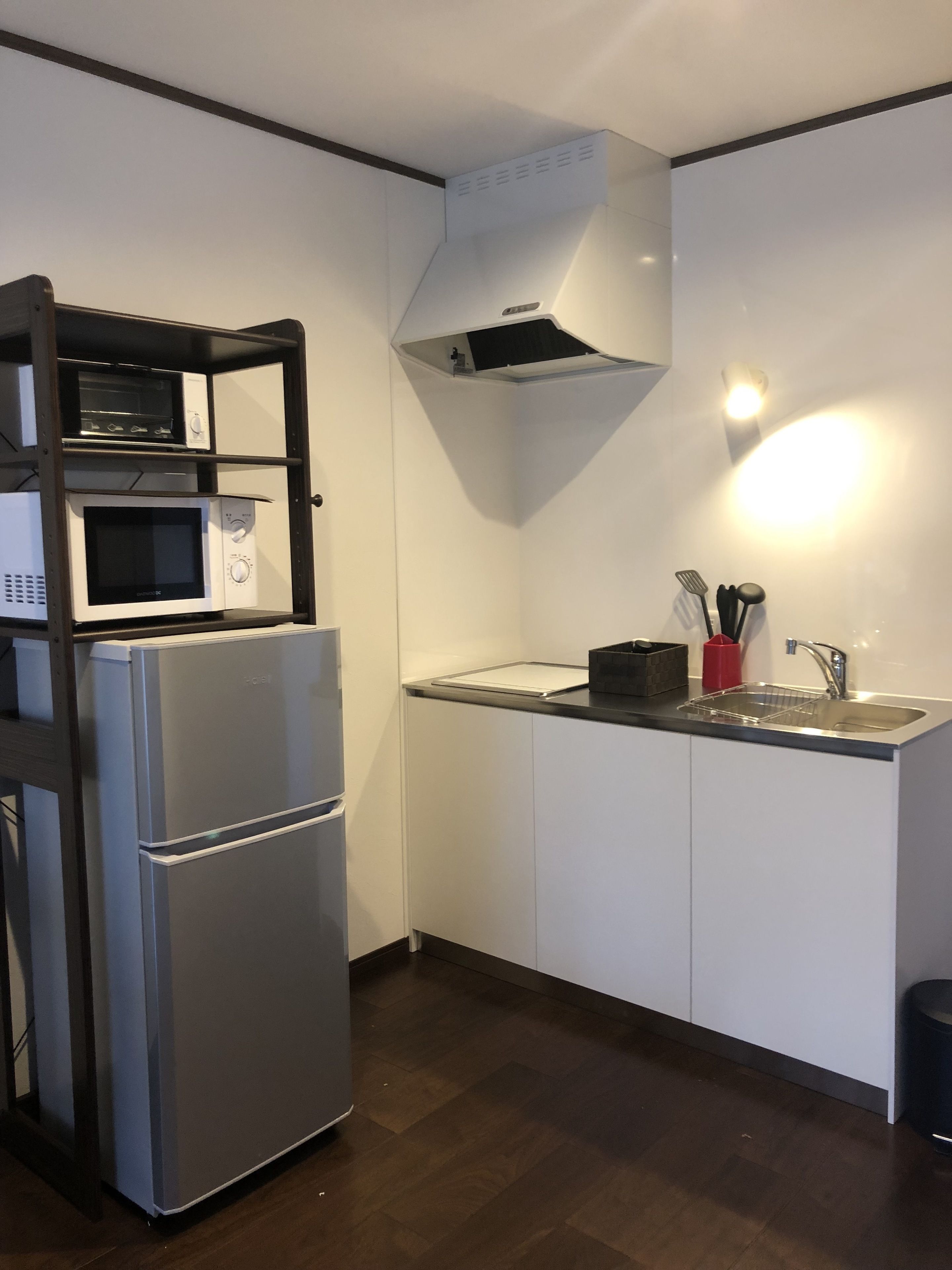 Een kleine keuken met een ingebouwde magnetron, oven en koelkast. Er is een wastafel met kraan en een klein aanrecht.