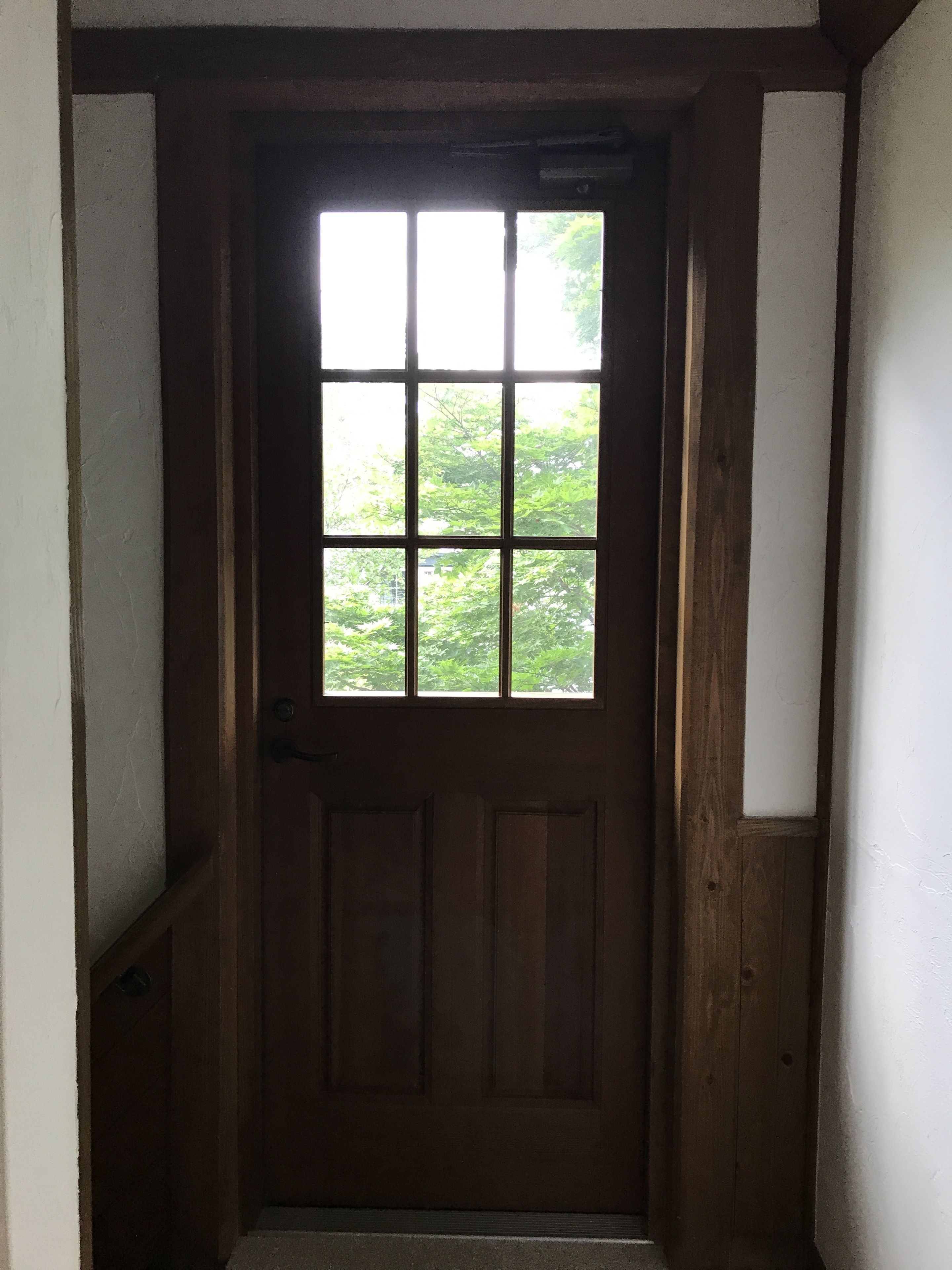 Eine Holztür mit Fenster, die zu einem Korridor mit weißen Wänden und einem sichtbaren Tritt führt.