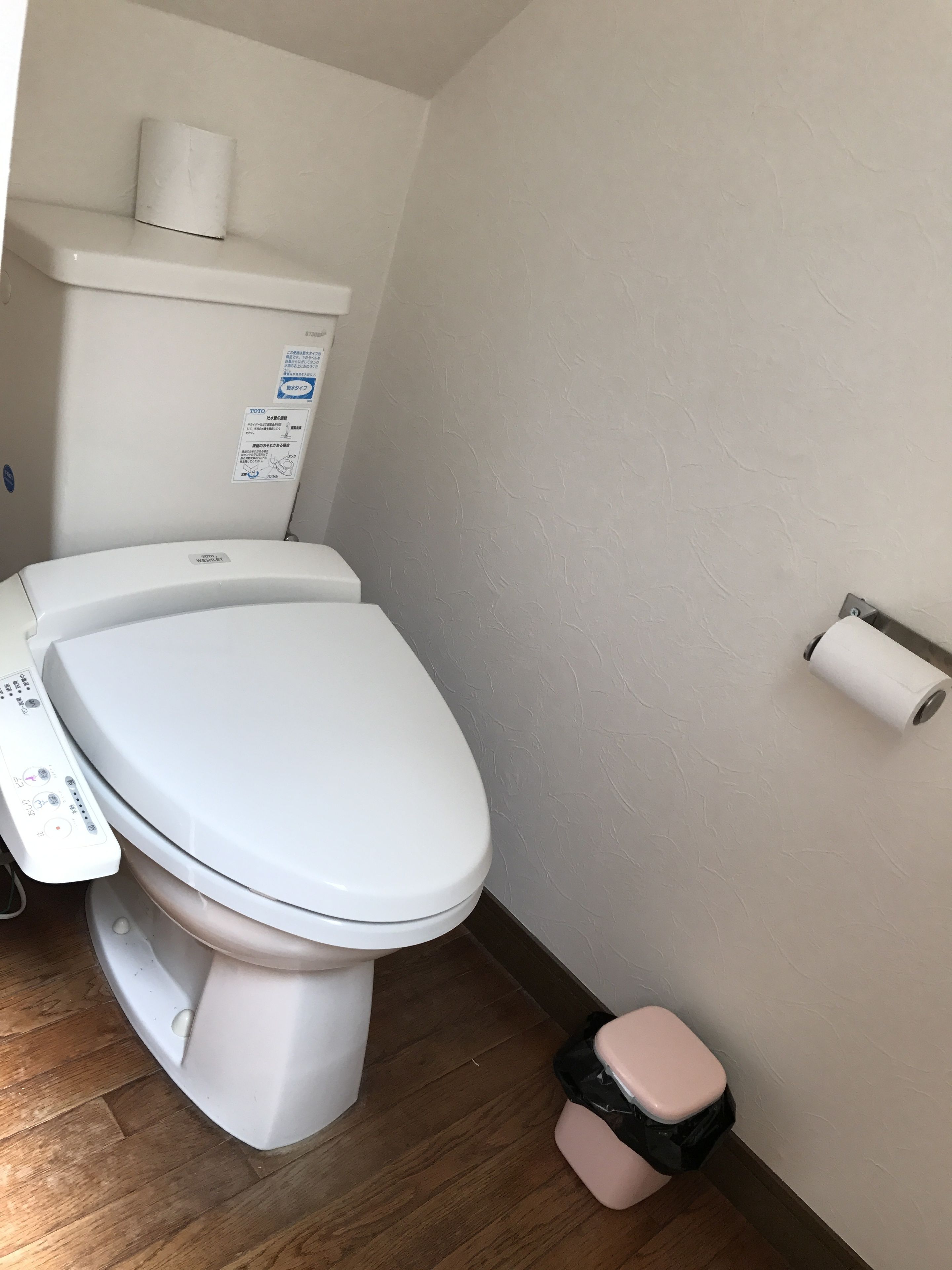 A white toilet with a control panel, a toilet paper holder on the wall, and a small trash bin.